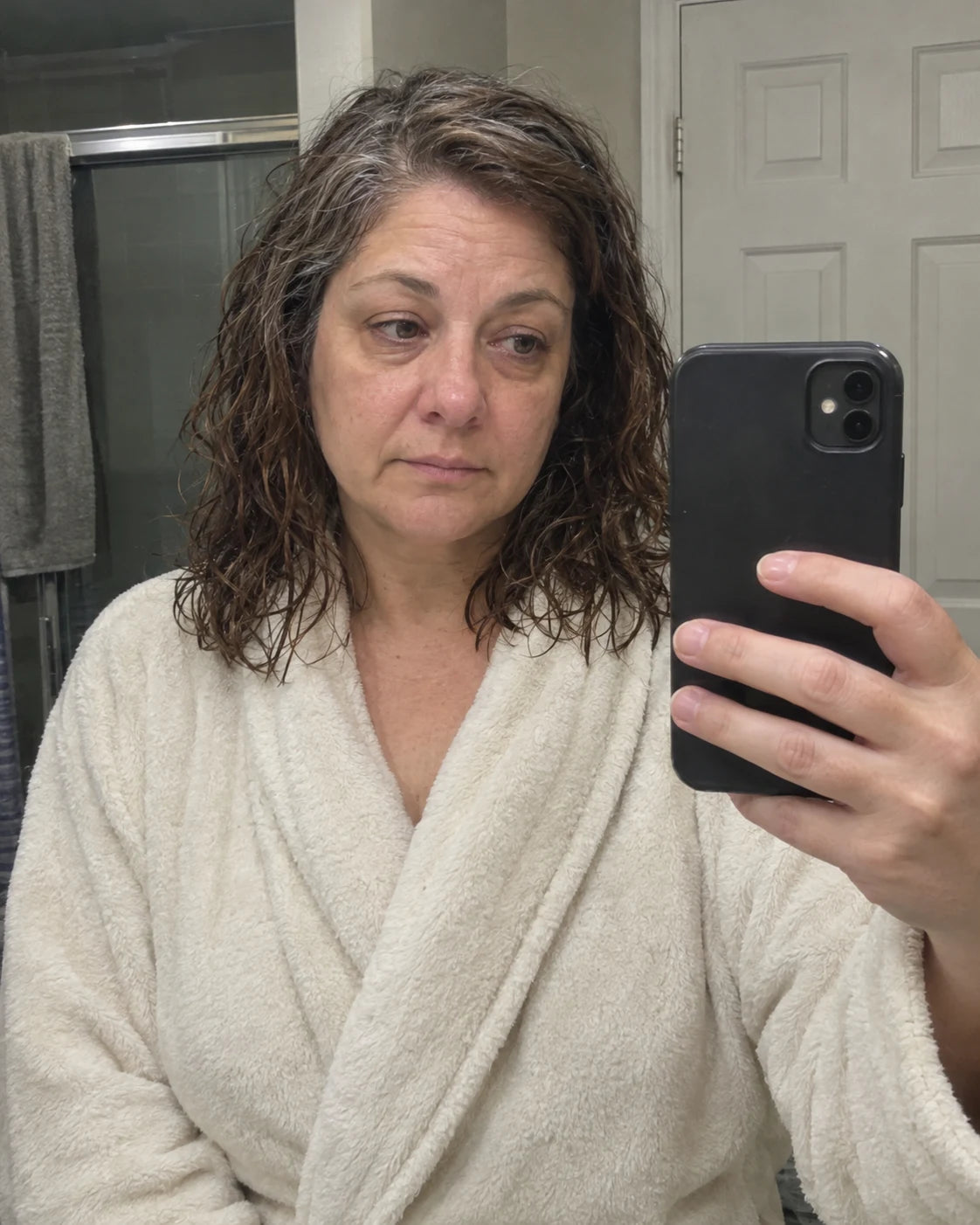 A tired woman taking a mirror selfie in her bathroom