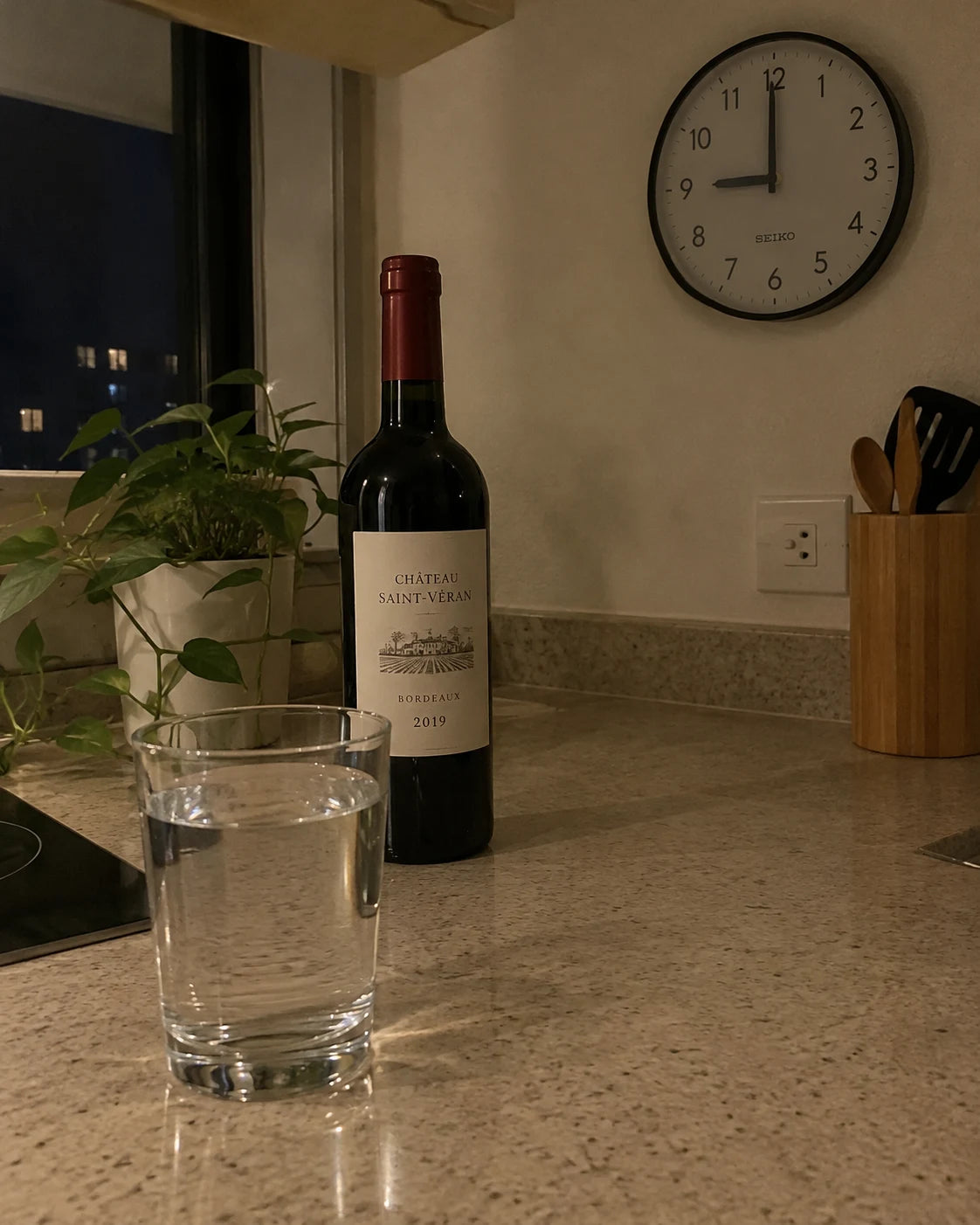 Unopened wine bottle next to a glass of water on a kitchen counter at night
