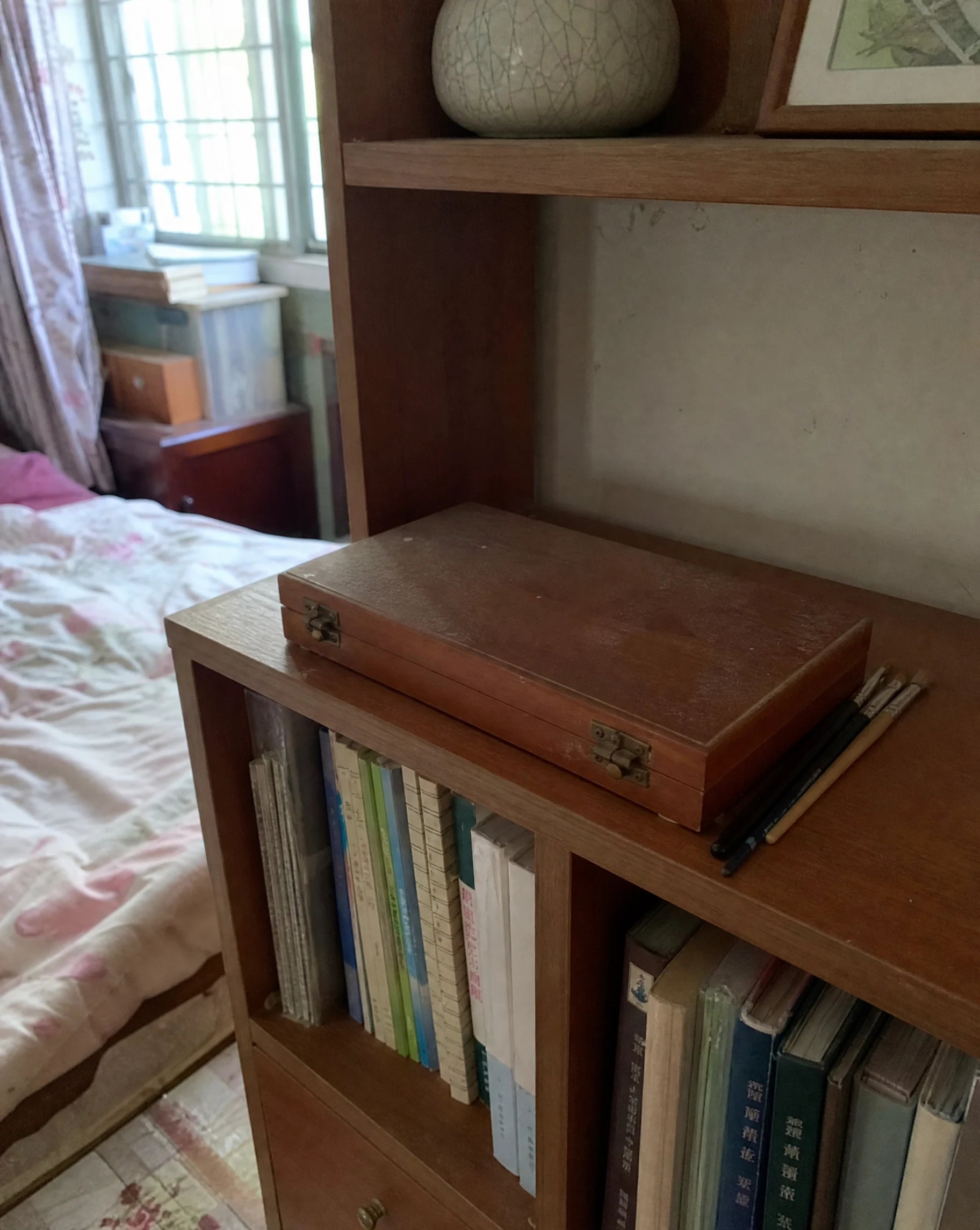 A small wooden box of watercolor paints sitting closed and dusty on a bedroom shelf