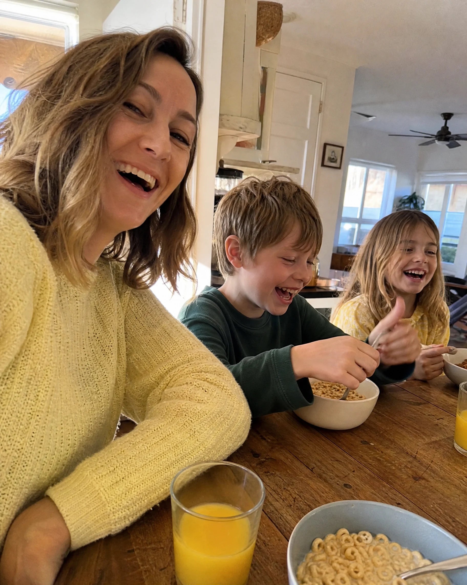 Mother laughing with her two kids at the breakfast table in morning sunlight, candid selfie
