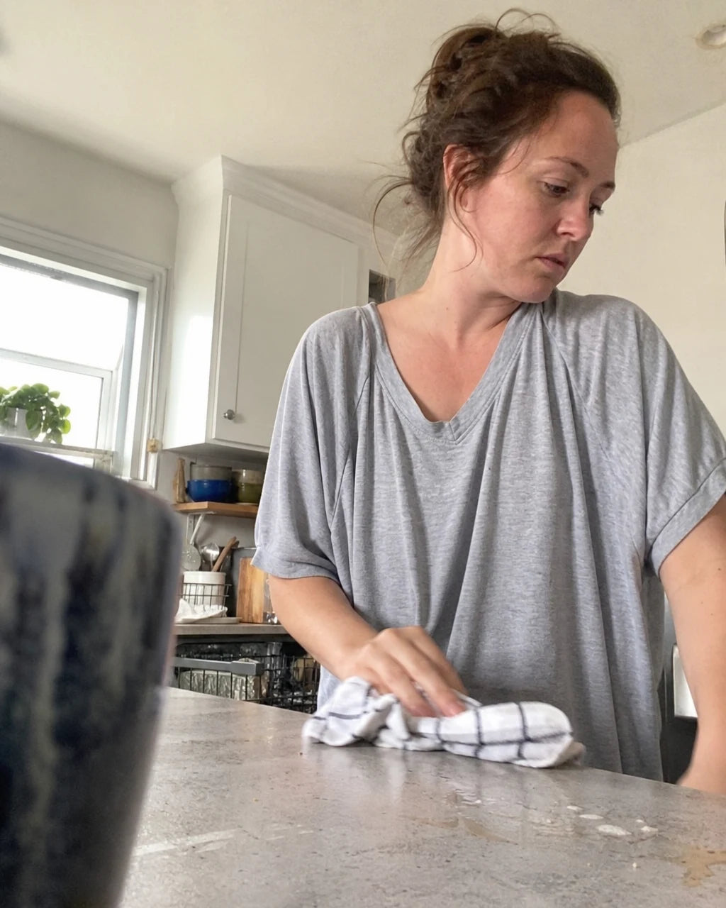 Woman half-asleep in pajamas wiping up a spill at the kitchen counter in the morning