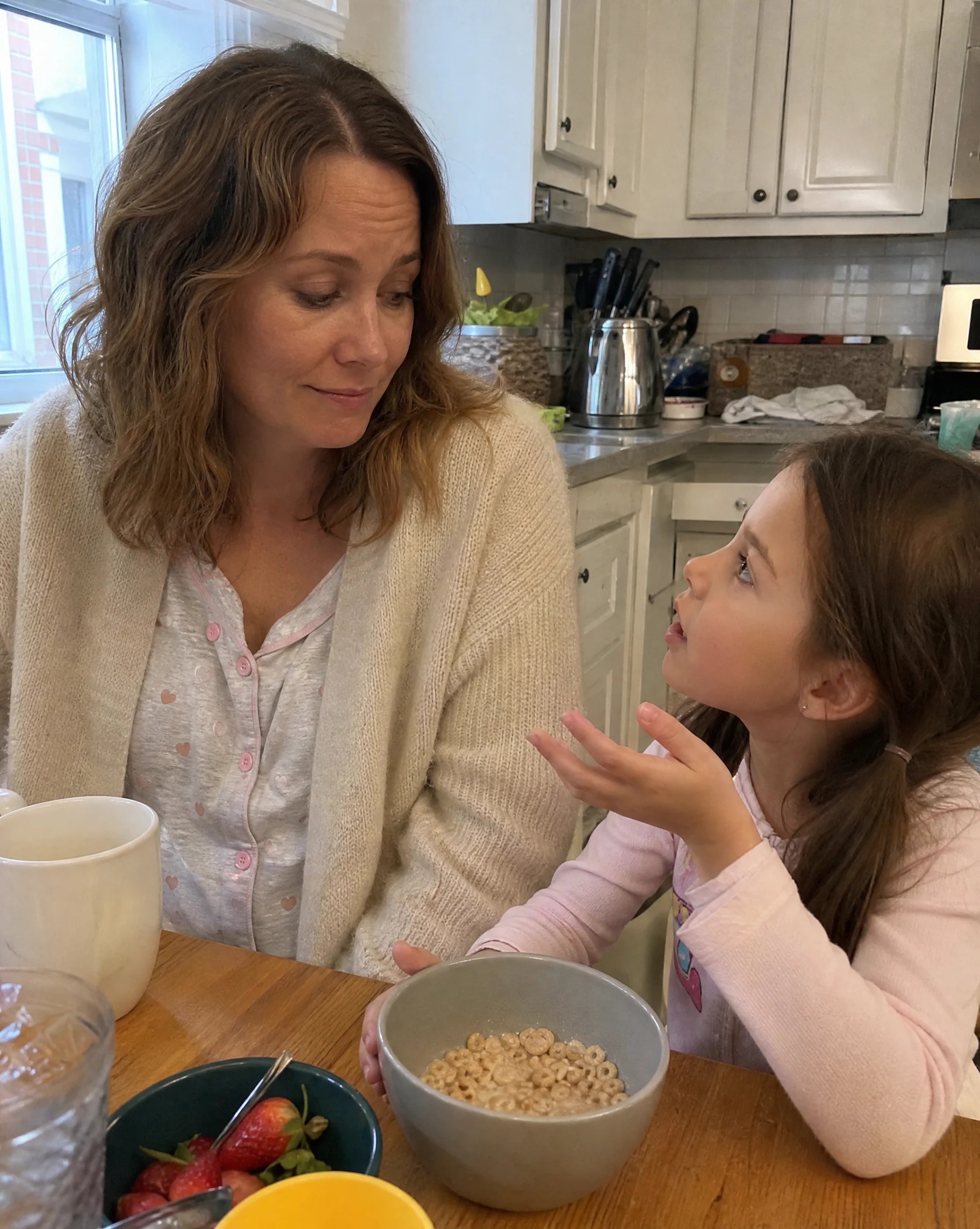 Mother and young daughter at the breakfast table, daughter asking a question, mother's smile fading