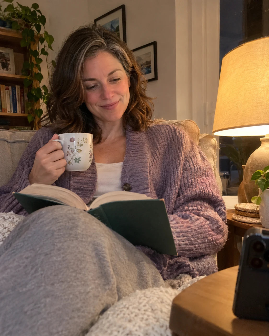 Woman relaxed on her couch in the evening with tea and a book, no wine