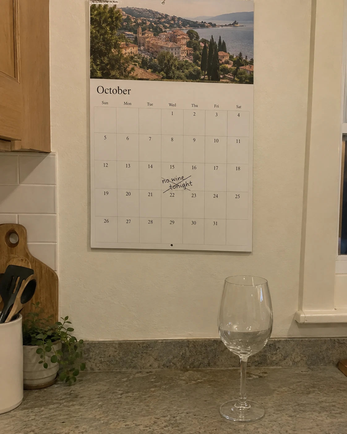 Kitchen calendar with a handwritten note 'no wine tonight' crossed out, next to an empty wine glass