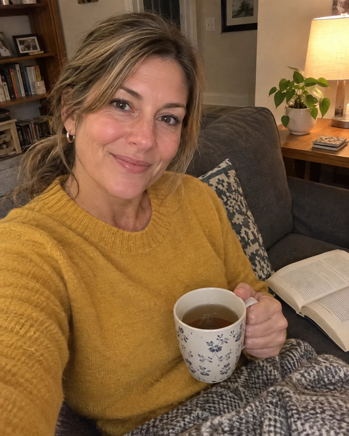 Woman relaxed on her couch in the evening with tea and a book, no wine, handheld selfie
