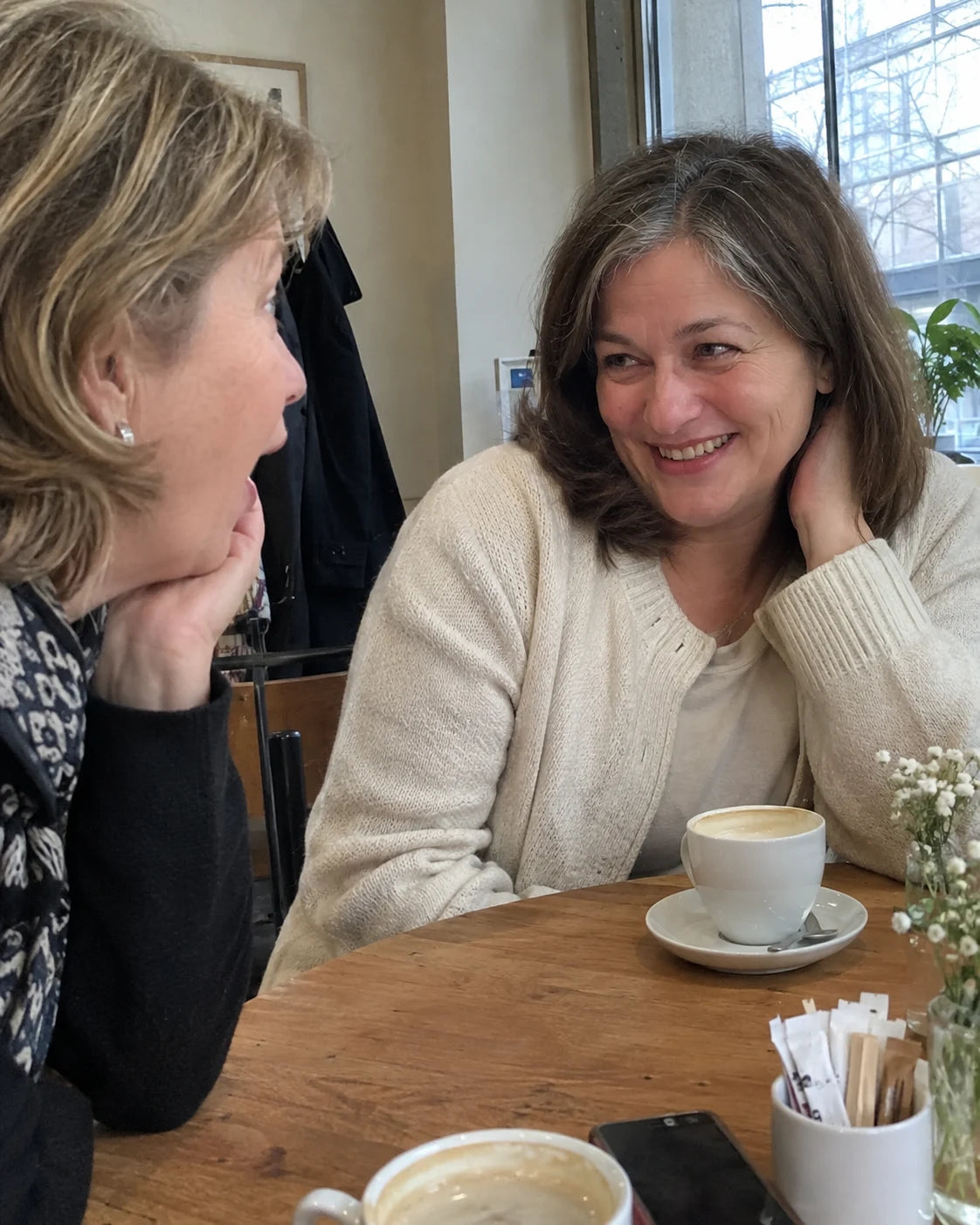 Two friends at a cafe table, one noticing a visible change in the other