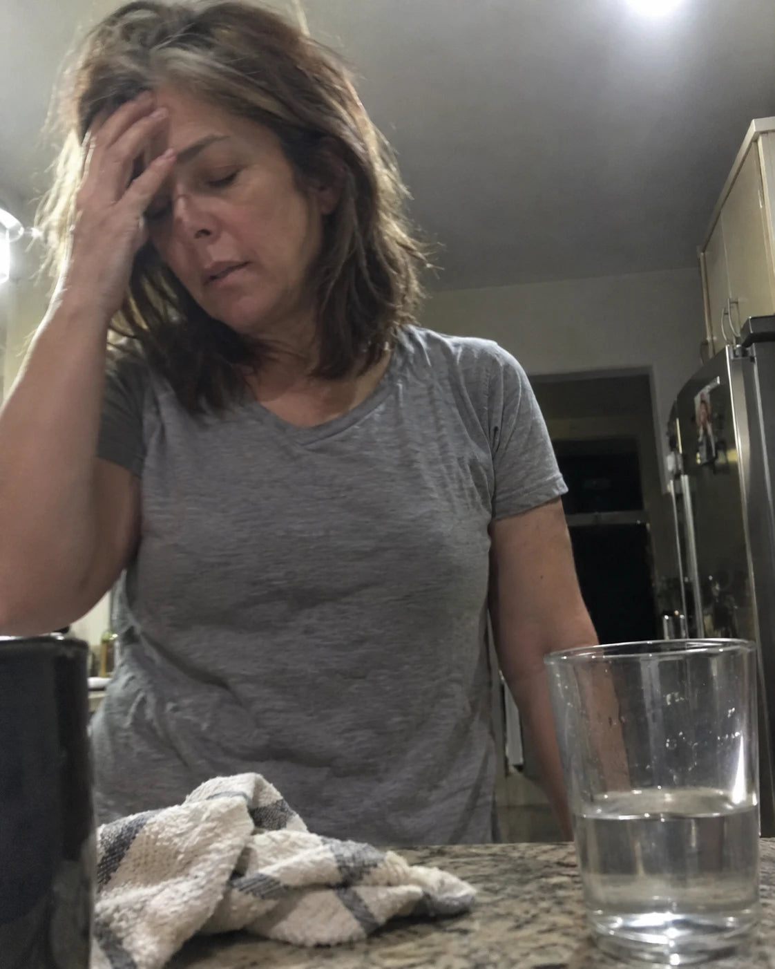 Tired woman standing at a dim kitchen counter late at night