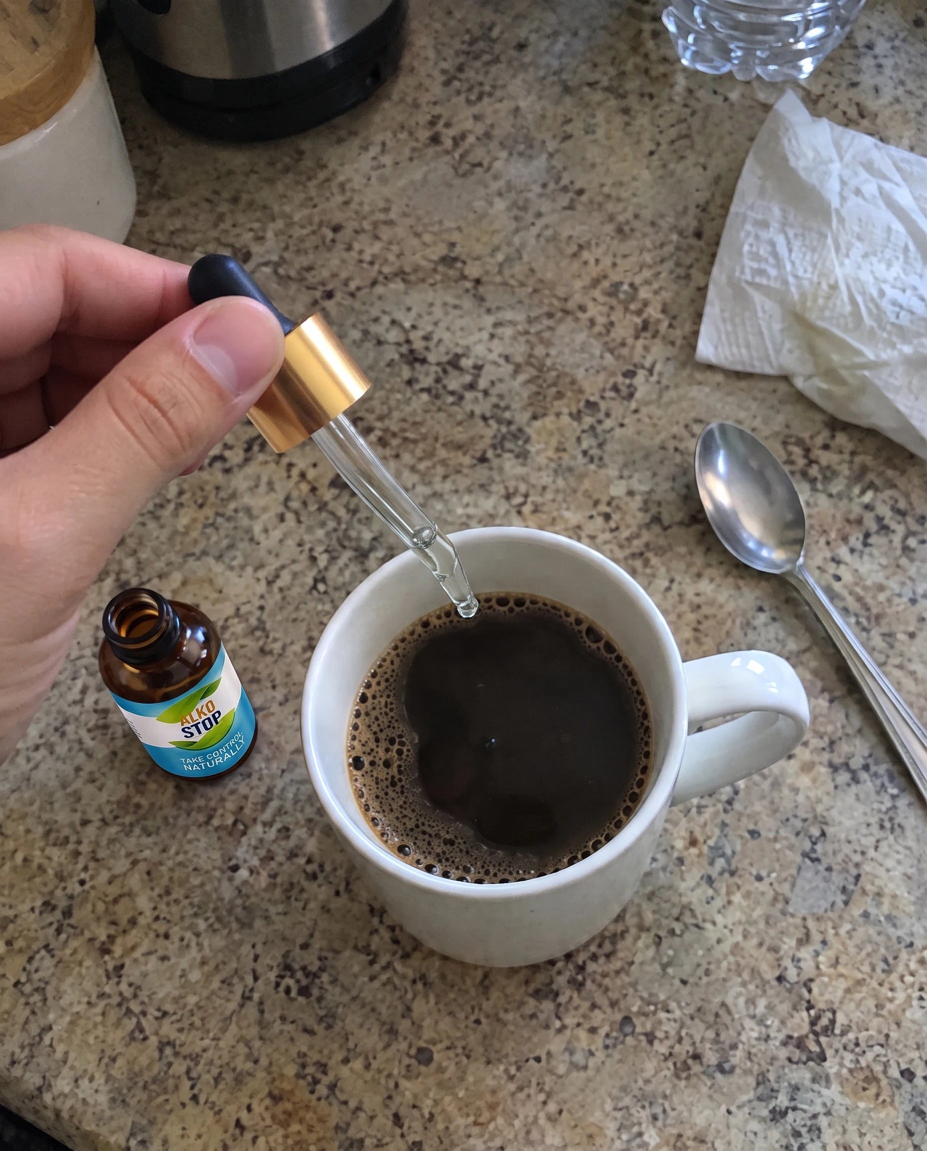 A hand adding a drop of AlkoStop into a cup of coffee