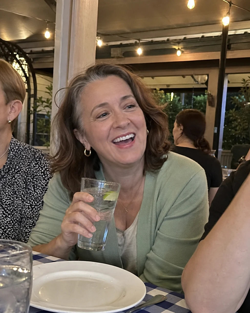 Woman laughing at dinner, holding a glass of sparkling water