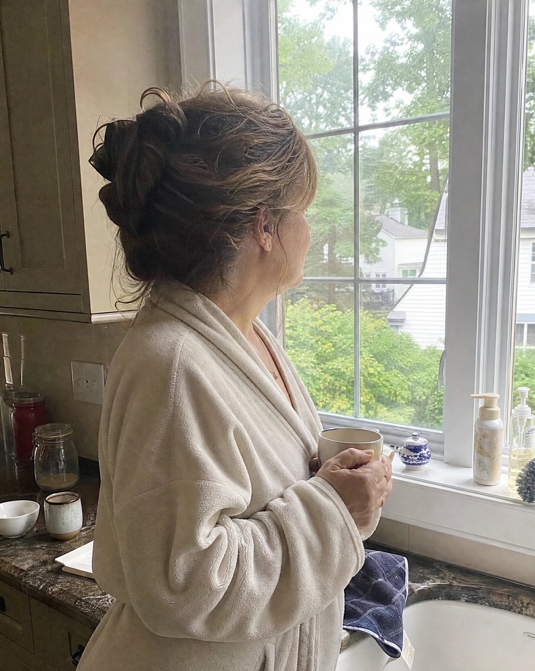 Woman standing alone at a kitchen window in the early morning