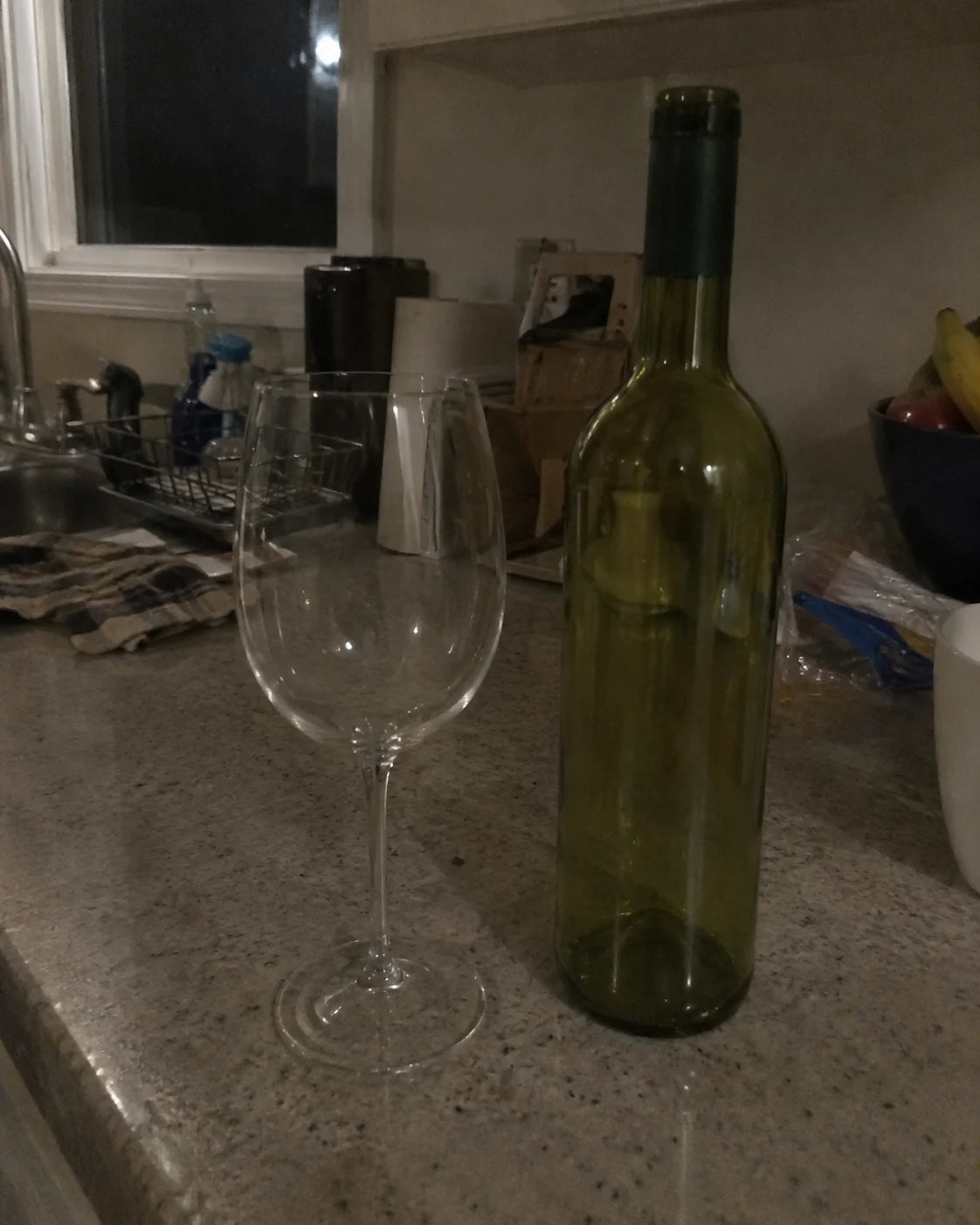 Empty wine glass and empty bottle on a counter at night