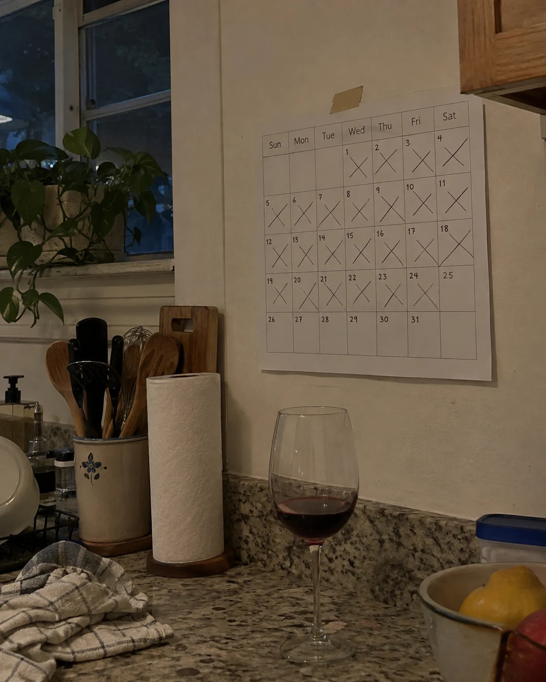 A kitchen calendar with most days crossed out, a wine glass on the counter below it