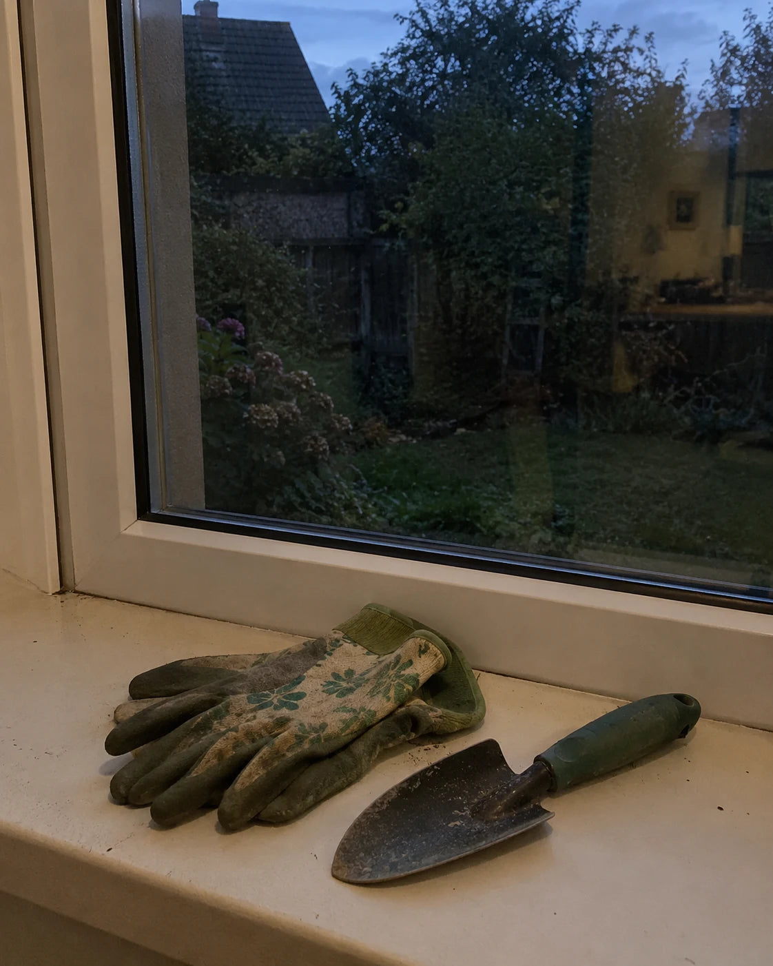 Gardening gloves set down untouched on a windowsill in the evening