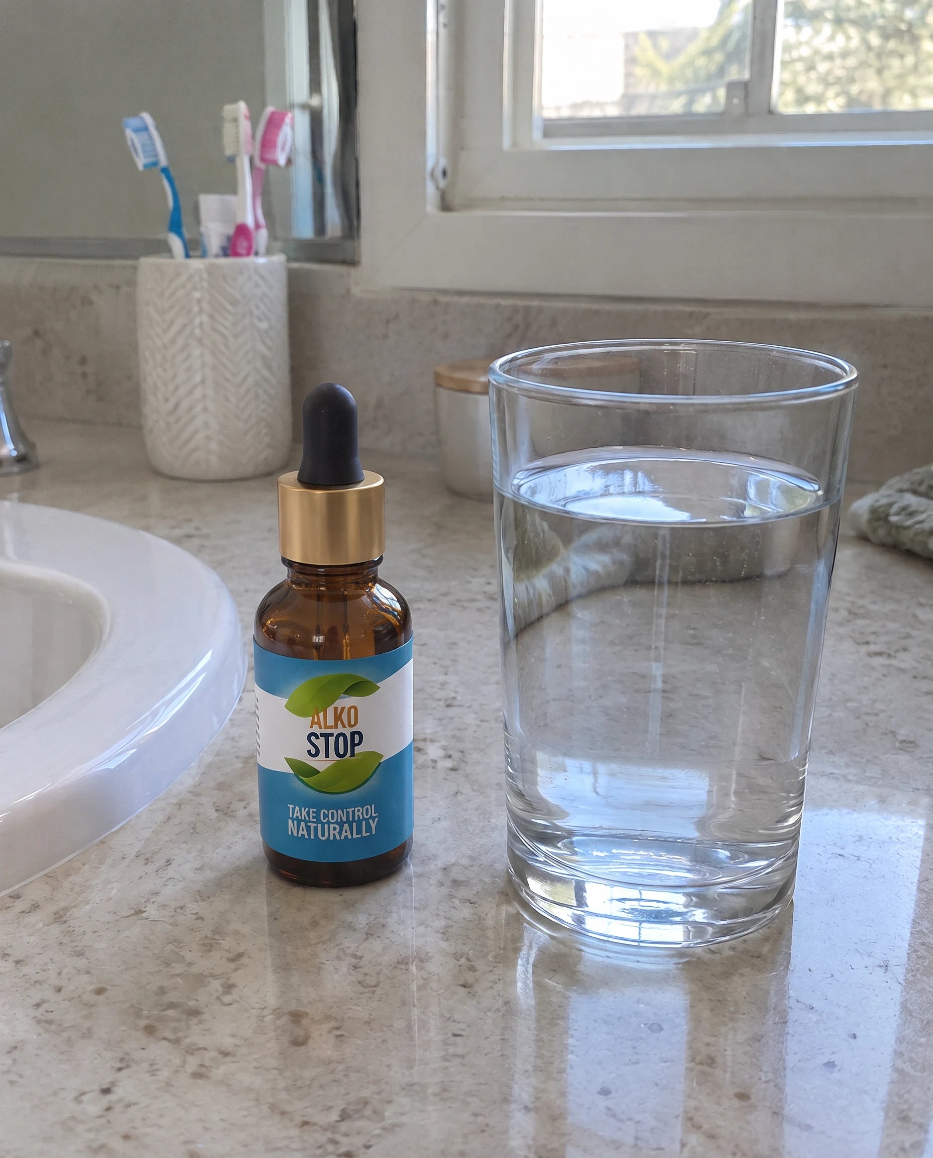 An AlkoStop dropper bottle next to a glass of water on a bathroom counter
