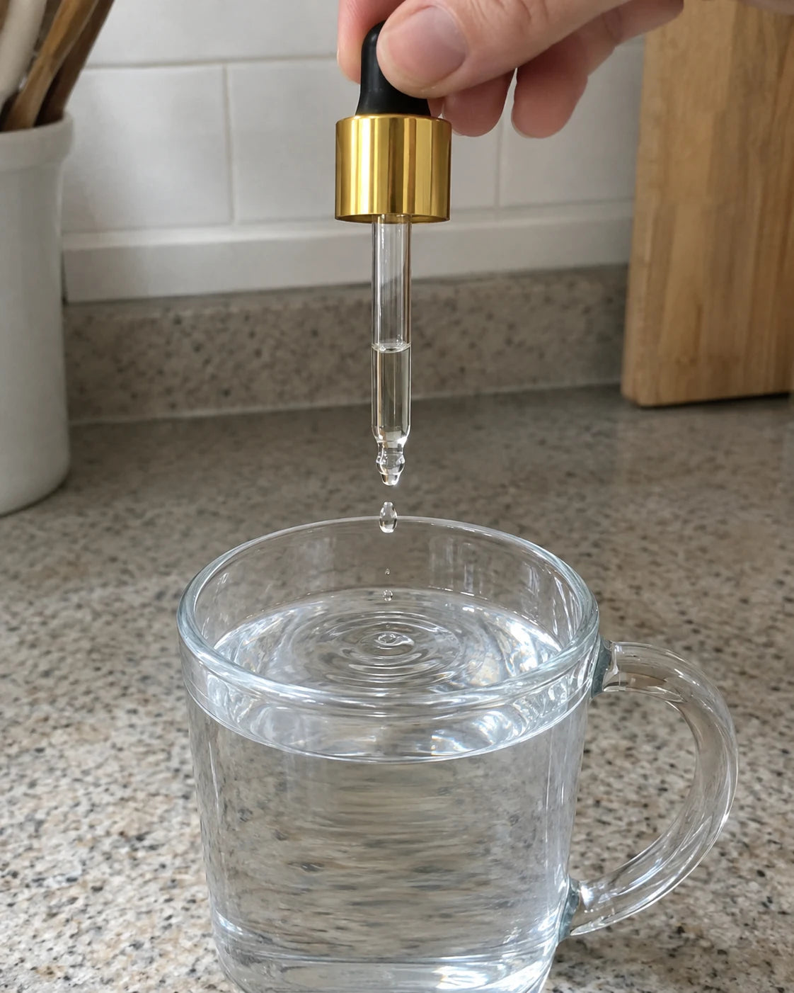 A single drop falling from a dropper into a mug of water on a kitchen counter