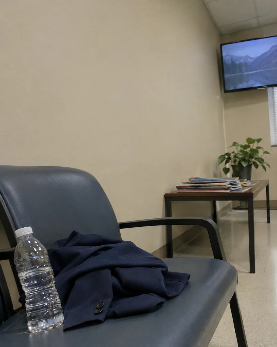 A water bottle and a folded blazer sitting on an empty doctor's office waiting room chair