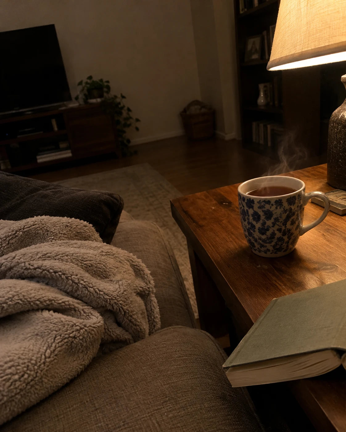 A steaming mug of tea on a side table next to a cozy blanket on the couch in the evening, no alcohol in sight