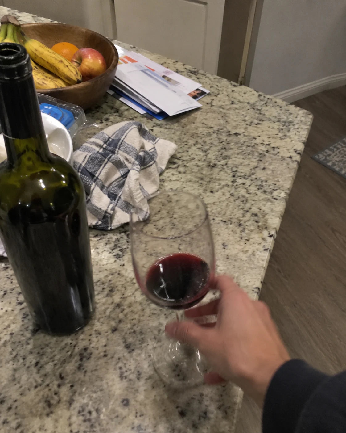 Hand reaching for a wine bottle and empty glass on a kitchen counter in early evening light