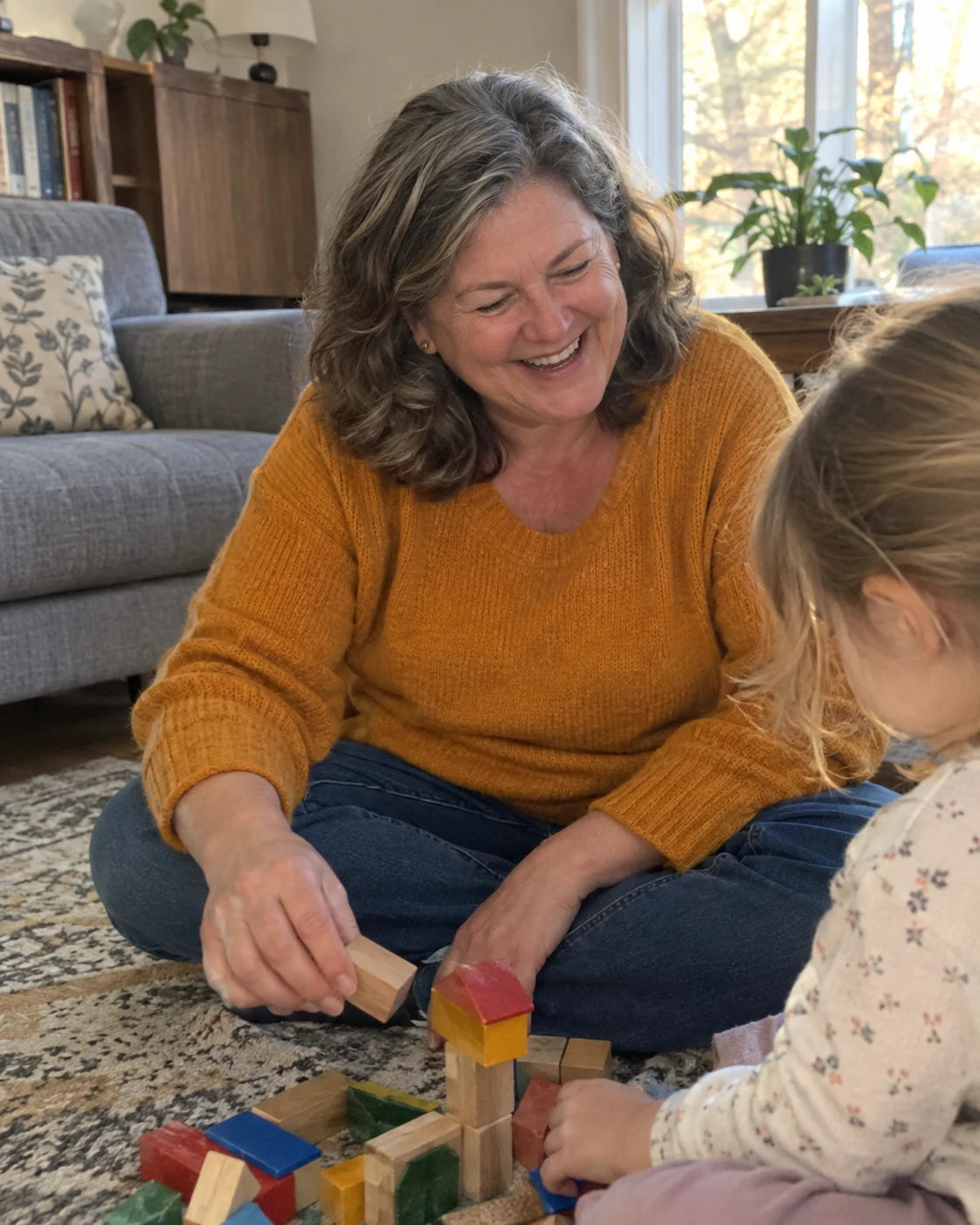Grandmother laughing, sitting on the living room rug playing building blocks with her grandchild