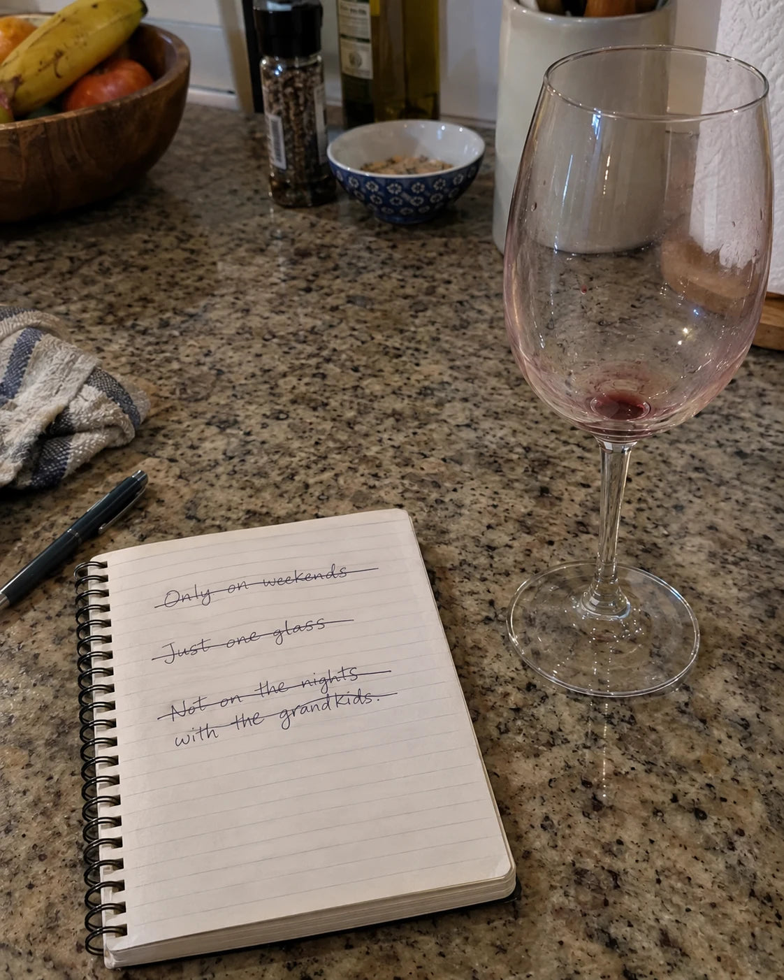 Handwritten notepad on a kitchen counter with personal drinking rules crossed out, next to a wine glass