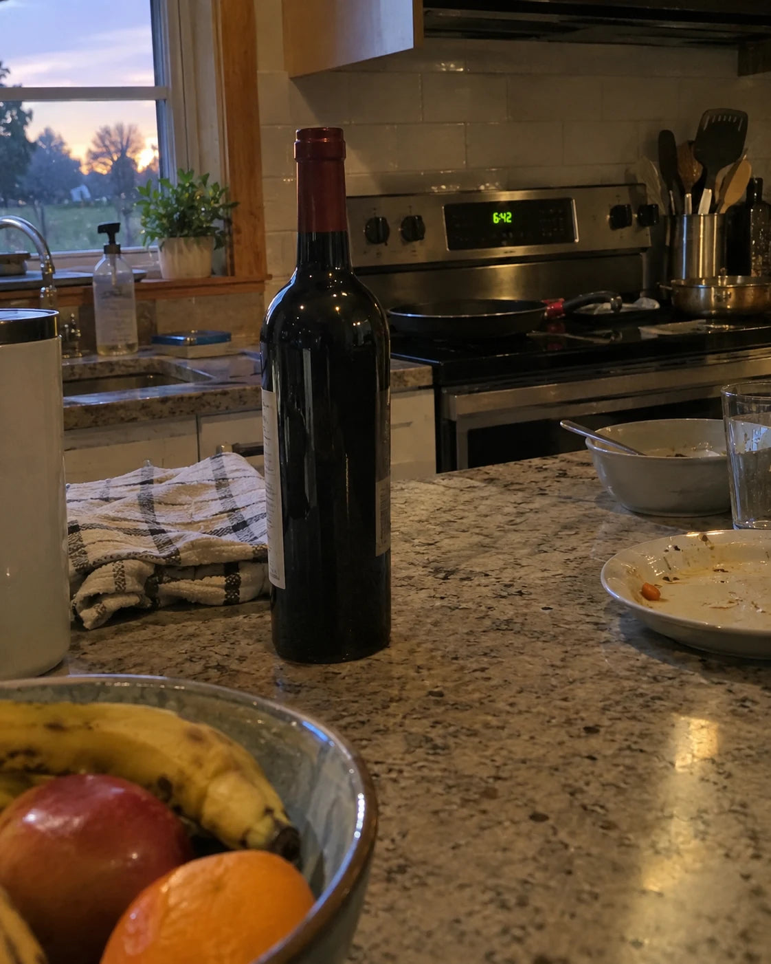 An unopened bottle of wine on a kitchen counter at 6:42pm