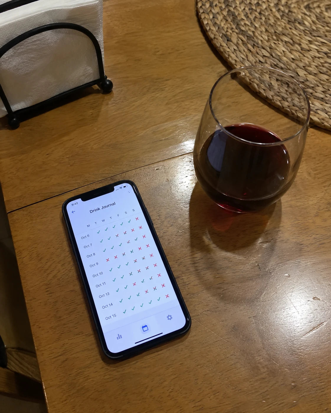 A phone showing a drink-tracking app next to a half-full glass of wine on a kitchen table