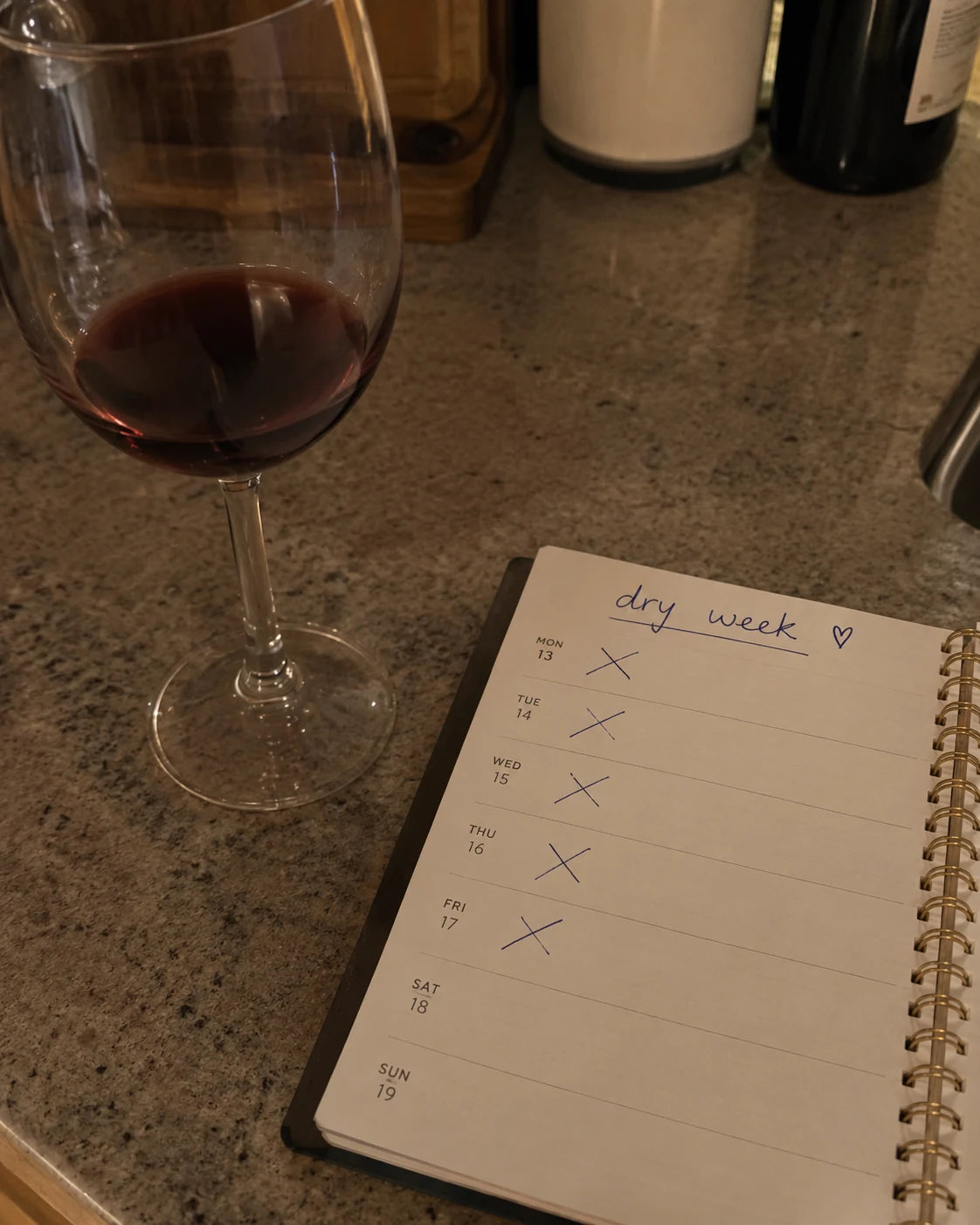 A wine glass next to a planner with dry week crossed out