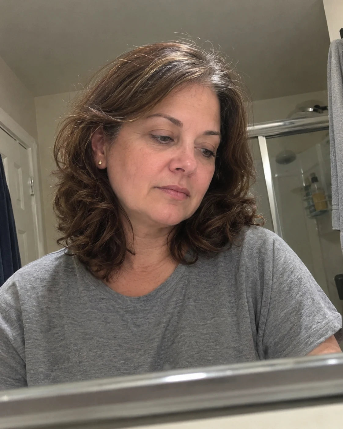 Woman alone in the bathroom mirror, reflective and tired