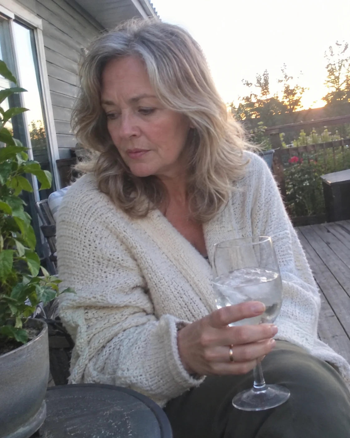 Woman holding a drink on an outdoor deck in early evening light