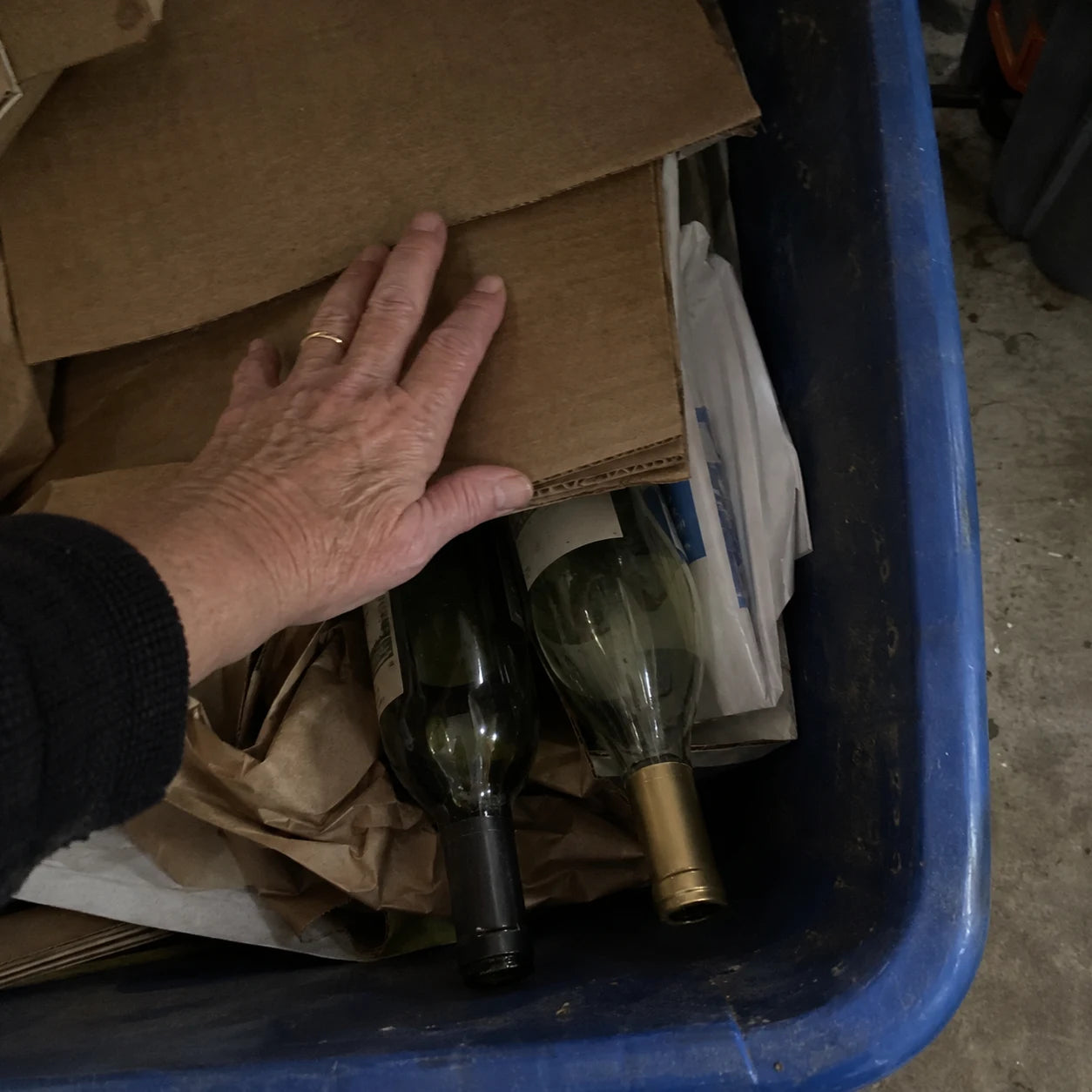 Hand hiding empty wine bottles in a recycling bin