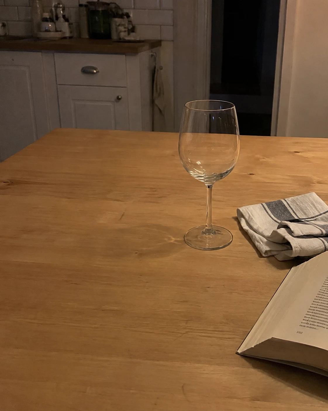 An empty wine glass pushed aside on the kitchen table in the evening