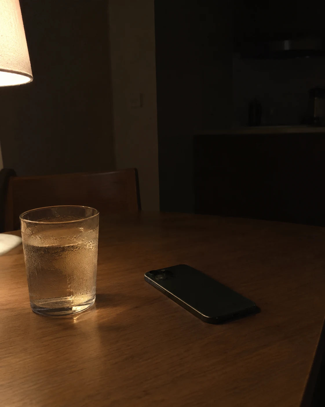 An untouched glass of water and a phone lying face-down on the table late at night