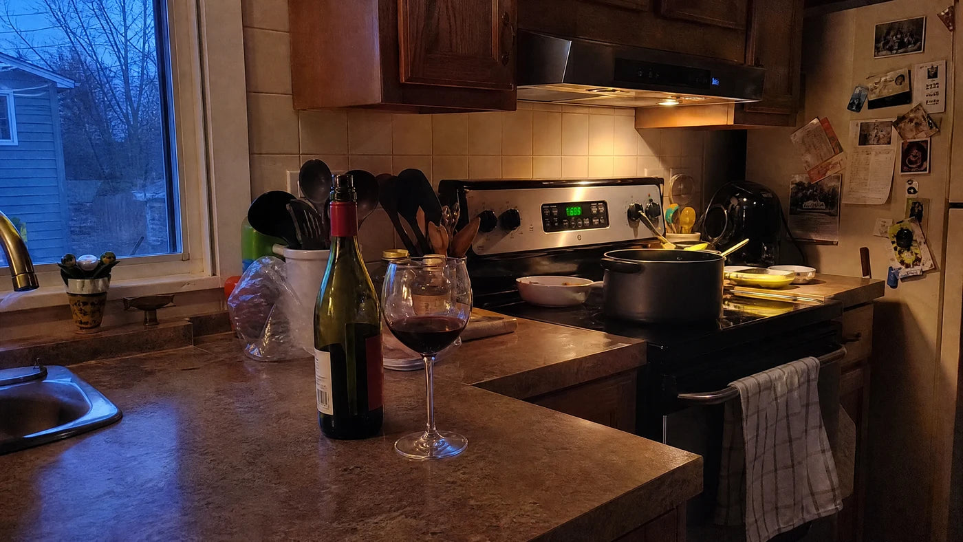 An open bottle of wine and a partly poured glass on a quiet kitchen counter at dusk