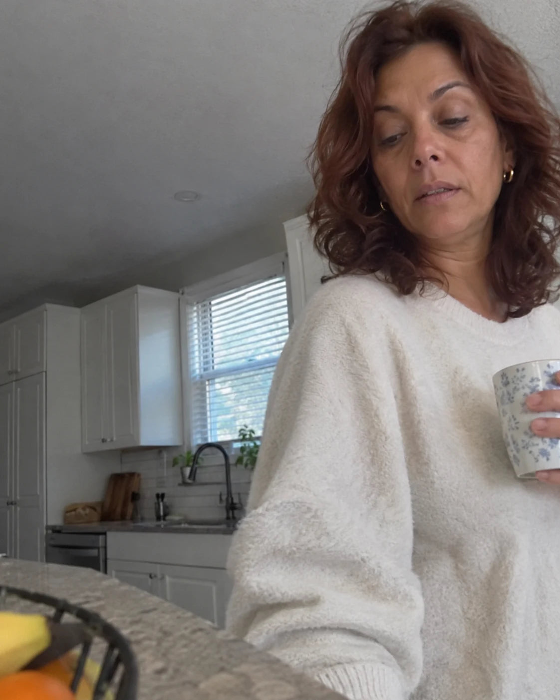 Woman looking groggy and foggy in her kitchen in the morning, holding a mug