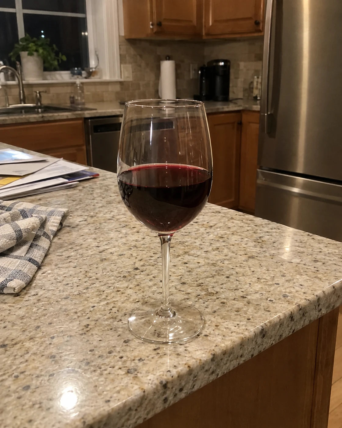 A single glass of red wine sitting alone on a kitchen counter at night