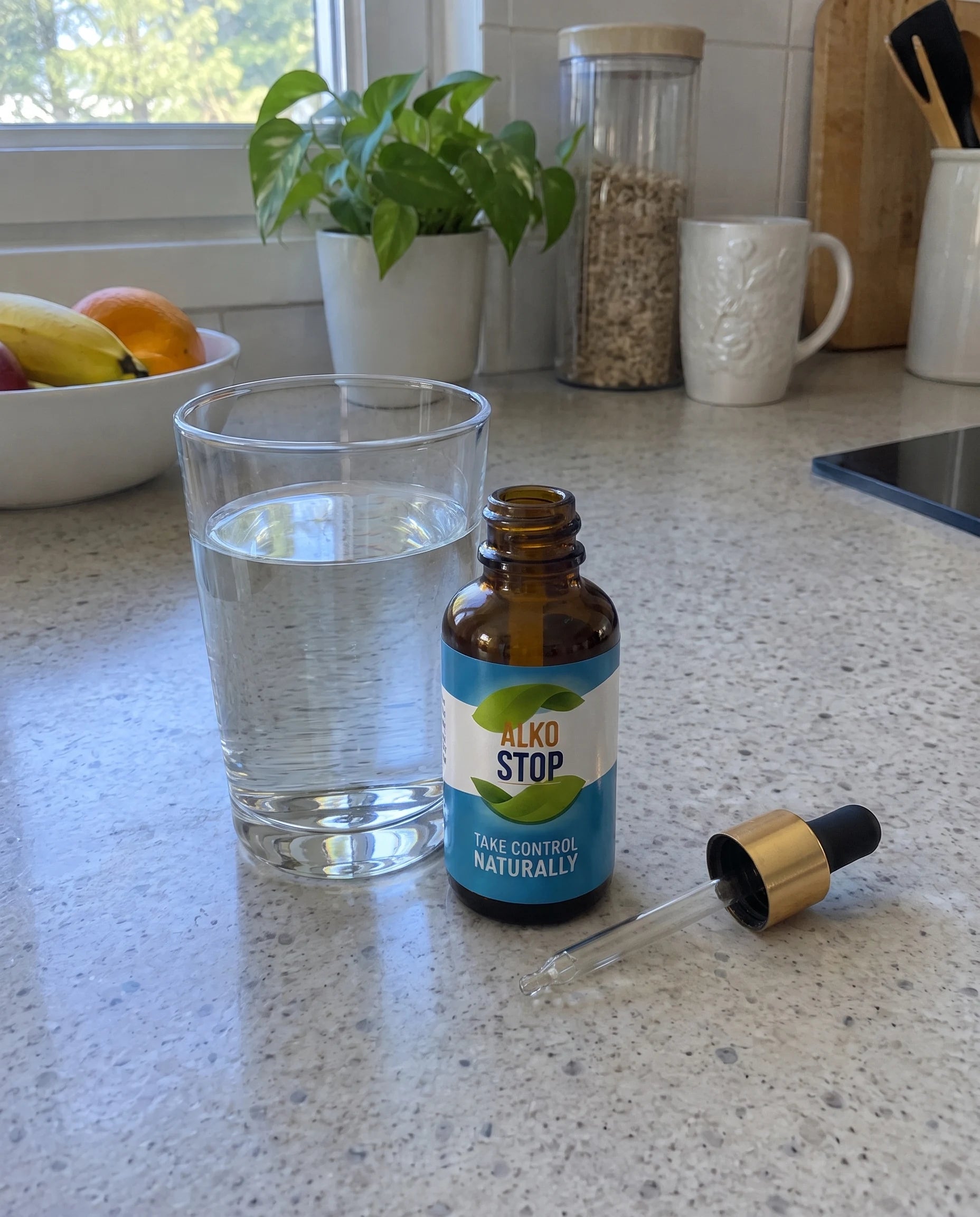 AlkoStop dropper bottle, open, beside a glass of water on a kitchen counter